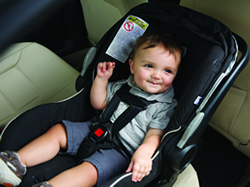 A toddler is buckled into a rear-facing child safety seat. 