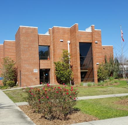 Image shows a brick building with a green lawn and empty sidewalks leading up to it. 