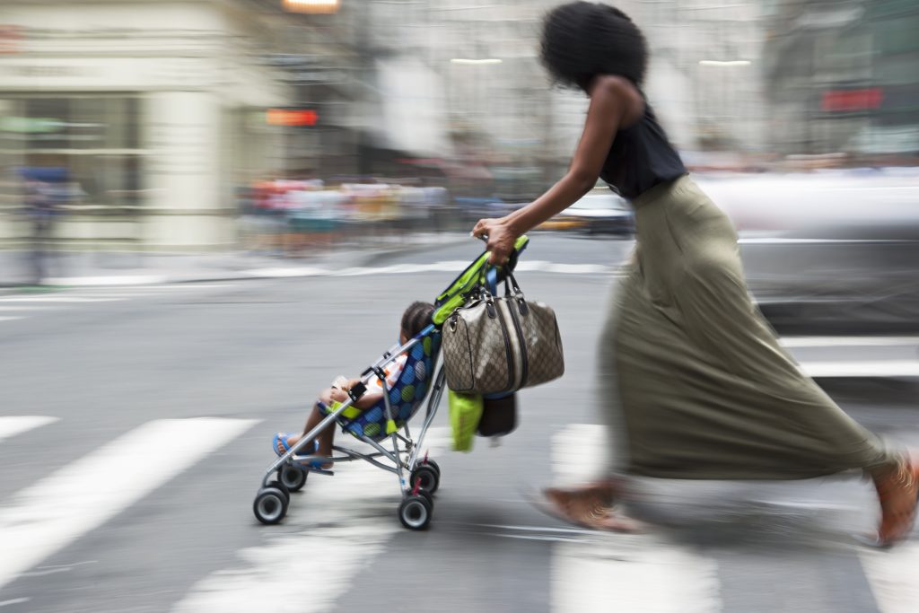 Woman pushing a child in a stroller through a crosswalk.